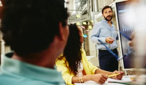 Tres compañeros de trabajo reunidos en una sala y revisando estadísticas y datos en una pantalla.