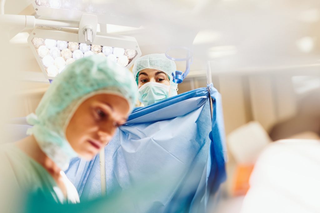 Two surgeons in sterile gowns and masks perform surgery under bright overhead lights in an operating room.
