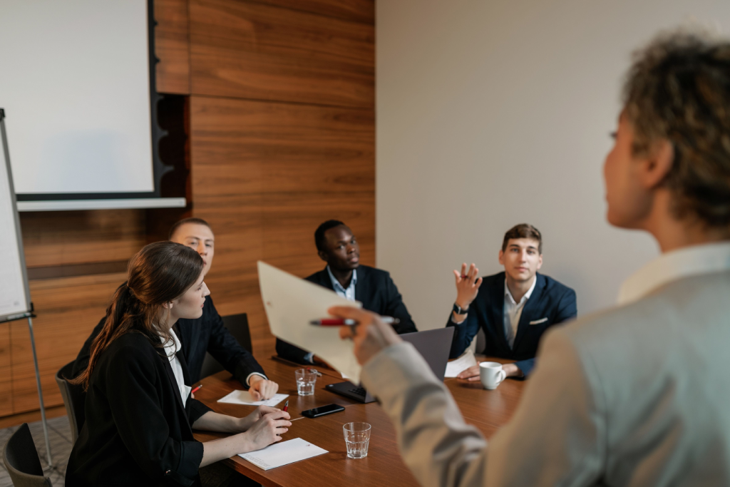 Diverse business team around a conference table, a presenter hands a document to attendees.