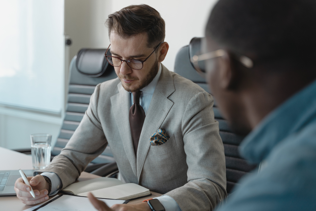 Professional man in a gray suit and glasses takes notes during a business meeting.