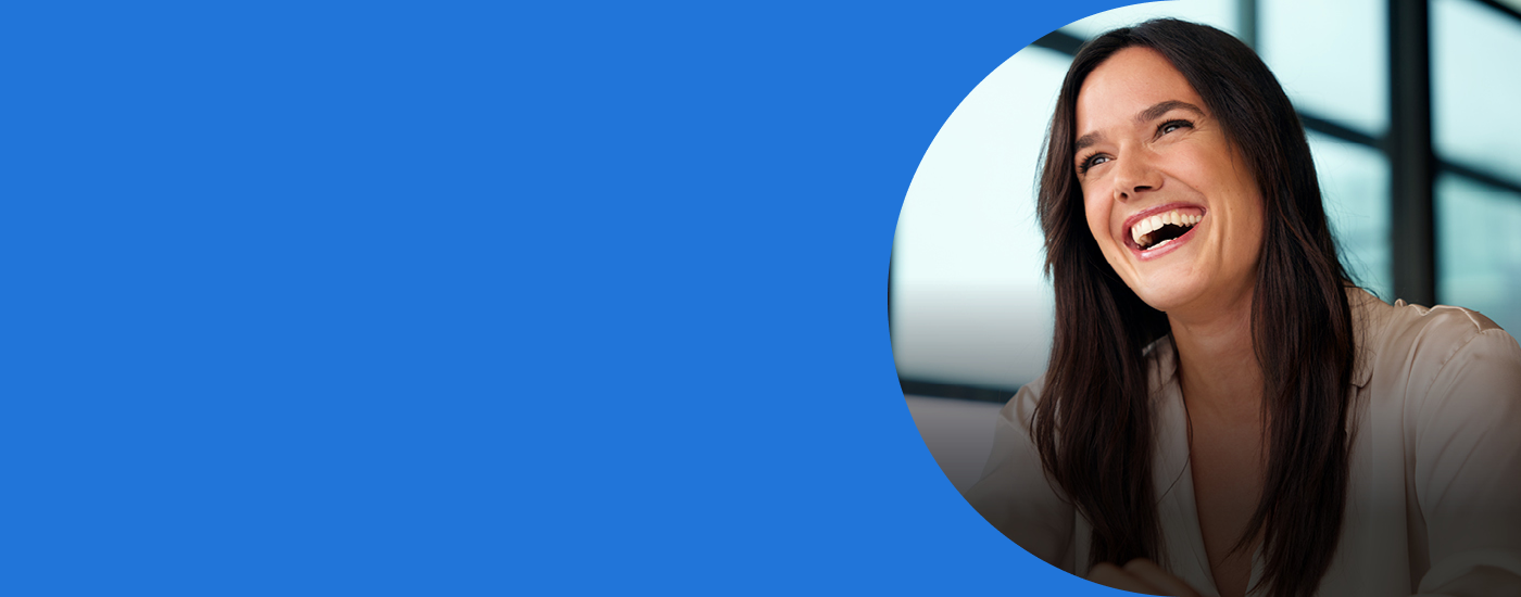 Smiling woman in a beige blouse seen through a curved blue cutout on a blue background, in an office setting.